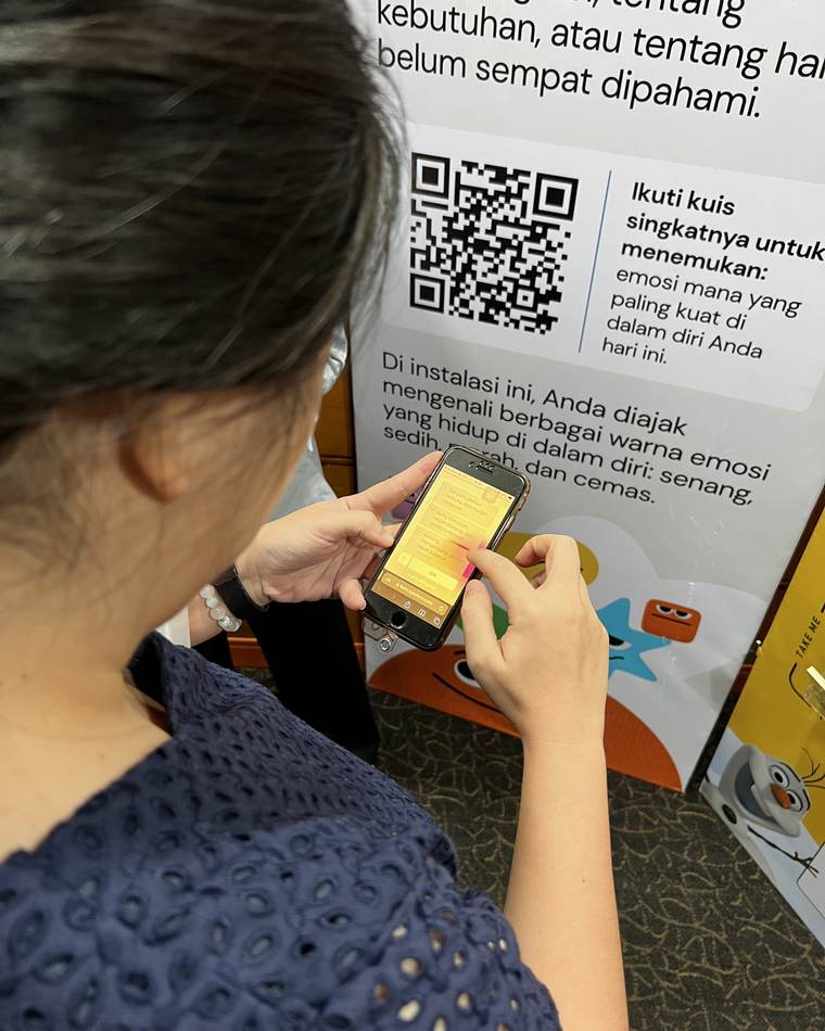 Seorang peserta memindai kode QR di panel instalasi interaktif tentang mengenali emosi.