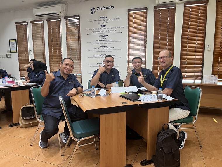 Empat peserta di meja diskusi, di dinding belakang tertulis mission, vision, dan core value perusahaan.